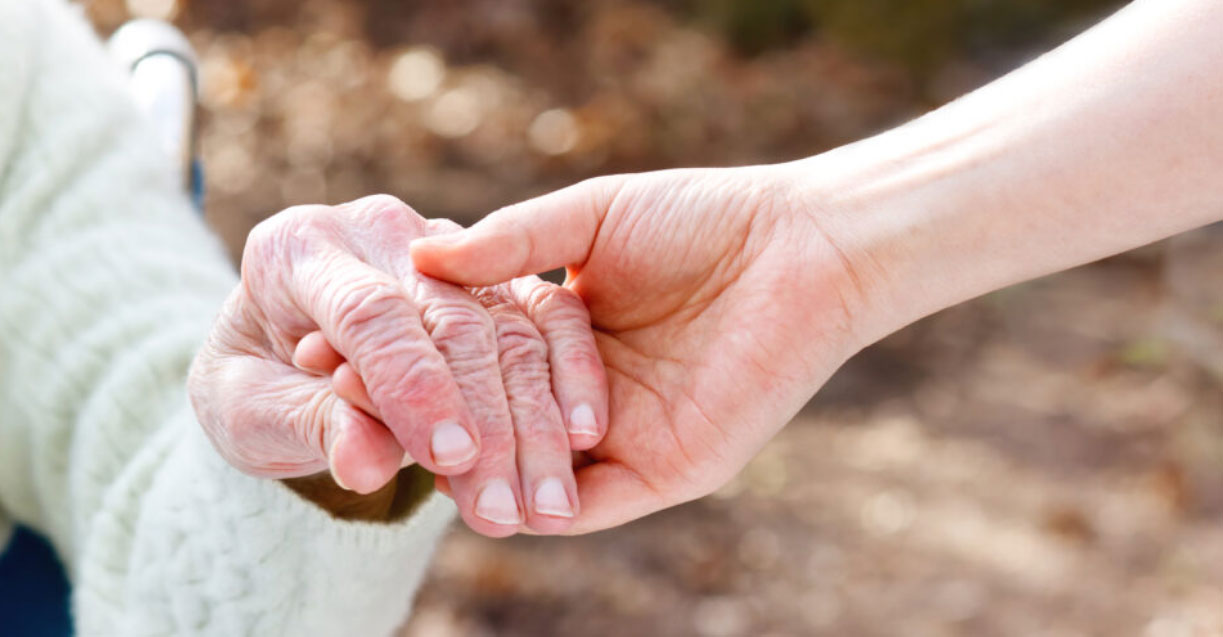 A young person holds the hand of an older relative