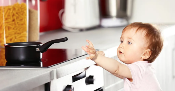 A baby reaching for a hot pan on top of the stove