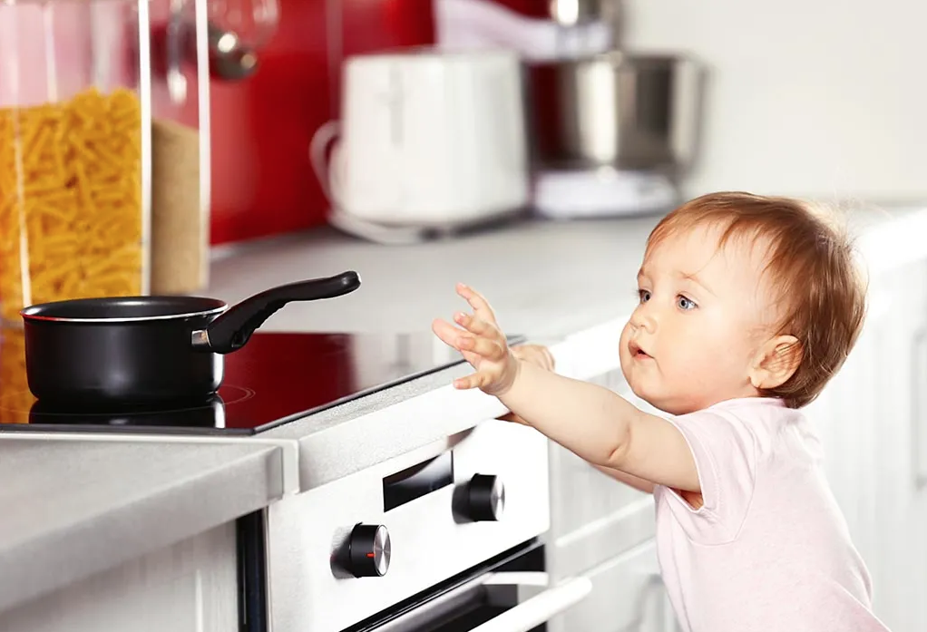 A baby reaching for a hot pan on top of the stove