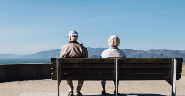 an elderly couple sits on a bench and looks at mountains