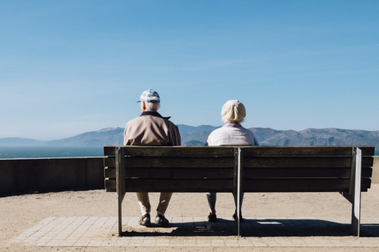 an elderly couple sits on a bench and looks at mountains